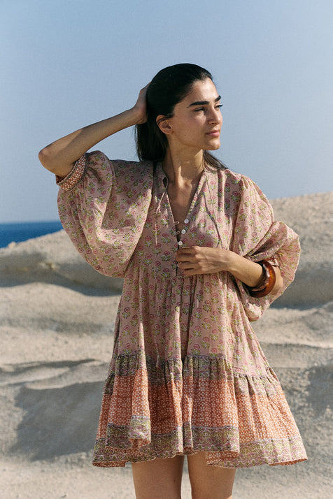 Woman on sandy beach dunes wearing the Daughters of India Bhoomi Mini Dress in Sunset, a peach and terracotta floral block print cotton mini dress with billowed sleeves