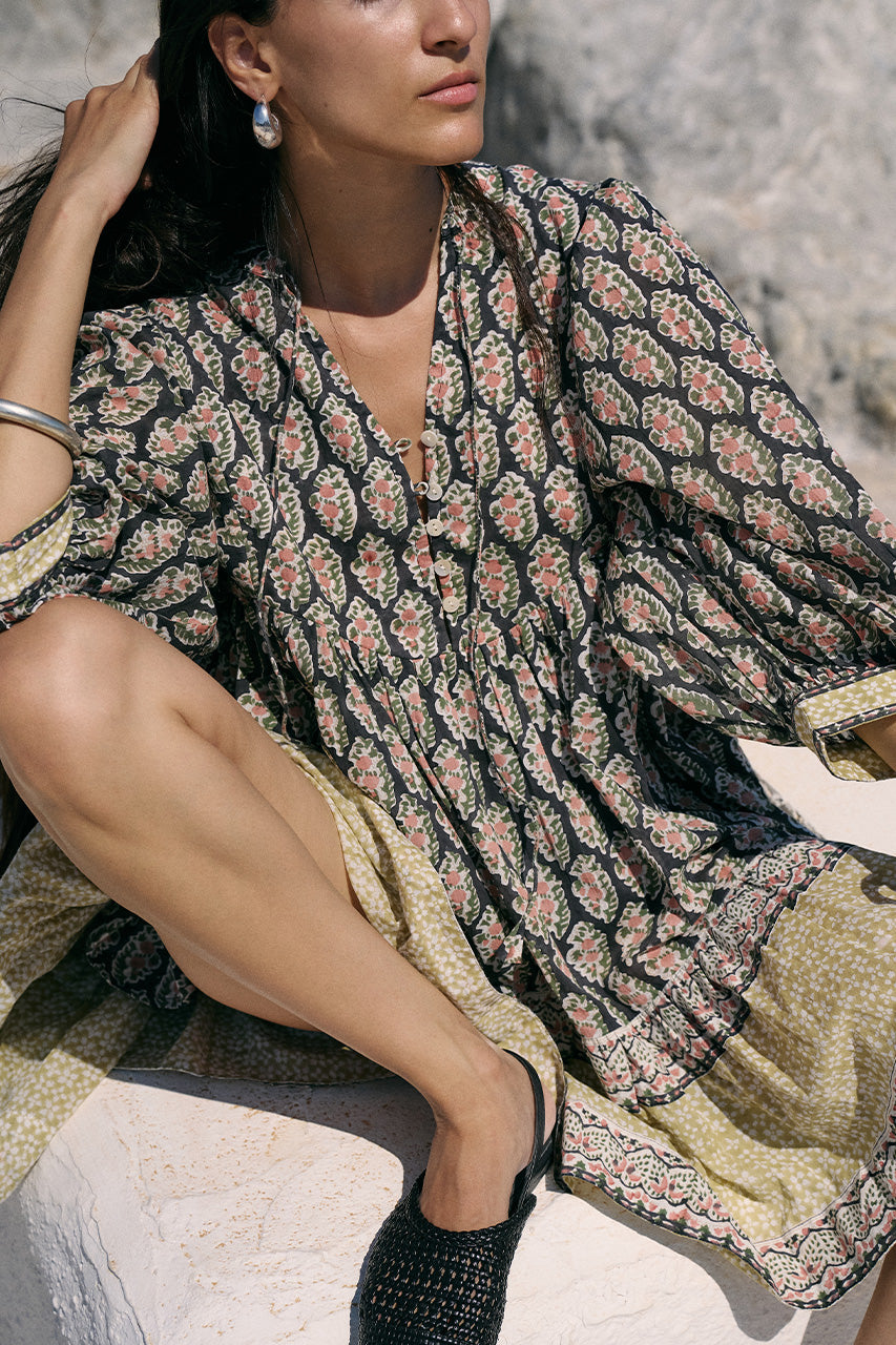 Close-up of woman seated outdoors wearing the Daughters of India Bhoomi Mini Dress in Onyx, showing the detailed paisley block print fabric and tiered skirt with border hem