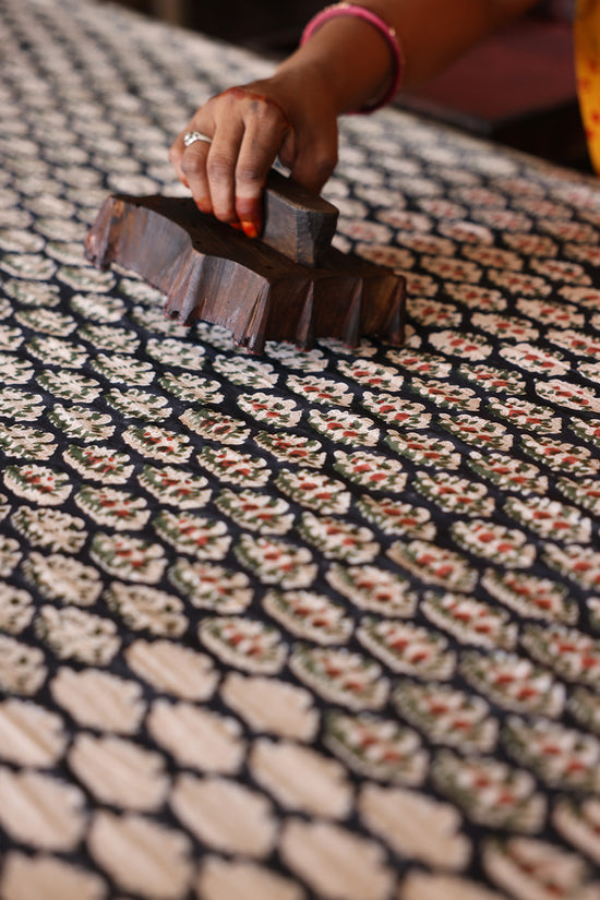 Indian artisan hand block printing the Onyx paisley pattern onto cotton fabric using a traditional carved wooden block, the craft behind Daughters of India Bhoomi Dress