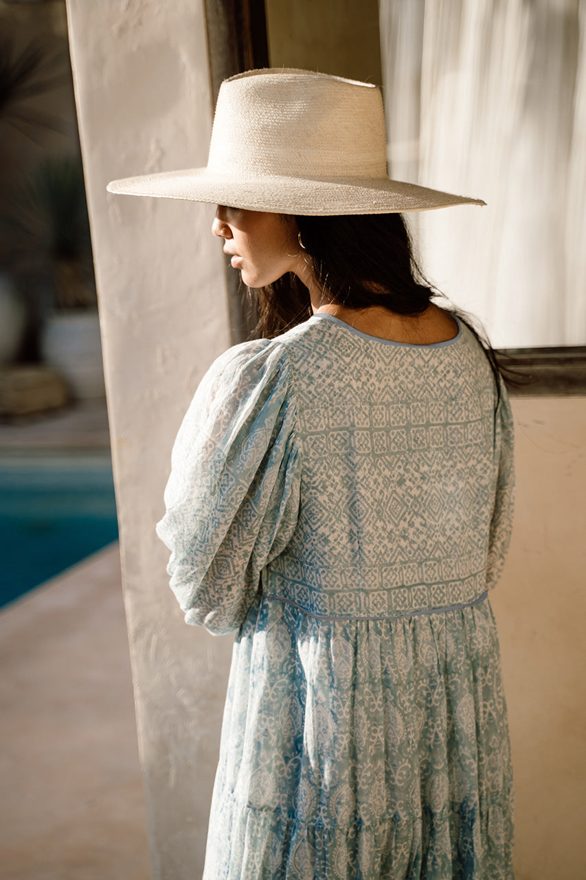 Jasmine Maxi Dress Sea Mist — back view with straw hat, riad archway with pool beyond, showing block print upper panel and tiered skirt, hand block print sea mist cotton, artisan Jaipur boho maxi | Daughters of India