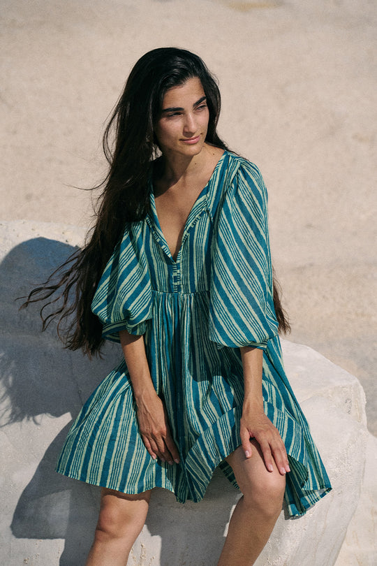 Woman wearing a green and blue striped dress on a sandy background