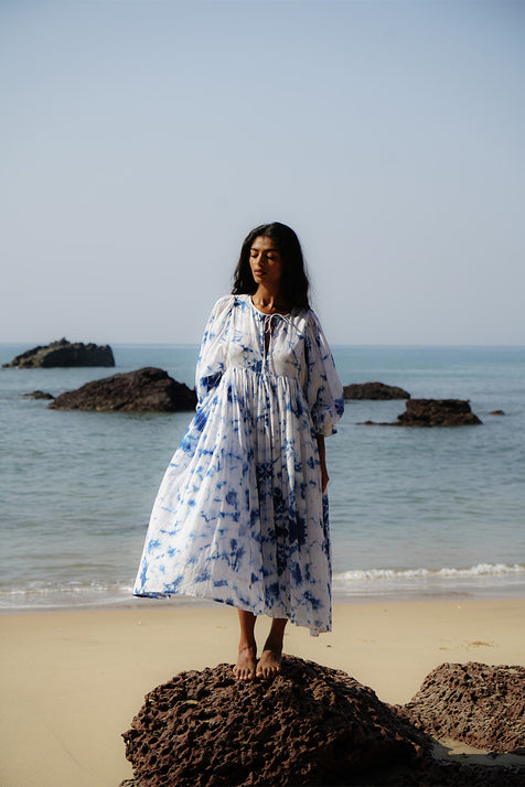 Kyra Midi Dress Deep Sea — full length front view standing on rocks at beach, deep sea shibori tie-dye cotton midi dress with V-neckline and balloon sleeves, ocean and rocks backdrop Goa India | Daughters of India