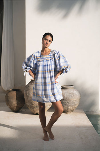 Freya Dress Periwinkle Blue Plaid — full length by terracotta pots and white walls, hand-smocked neckline, billowy sleeves, handloom woven periwinkle blue plaid mini, artisan boho dress | Daughters of India